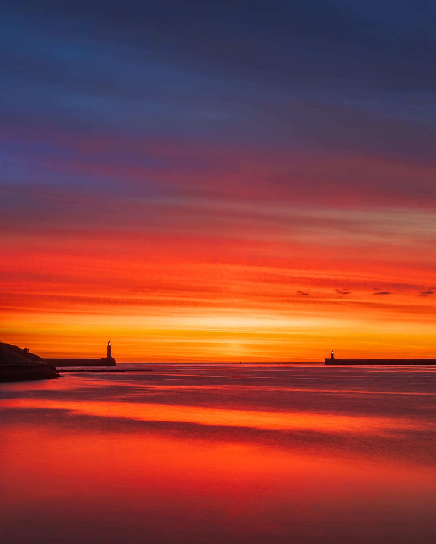 Fiery sunrise showing Tynemouth and South Shields lighthouses.