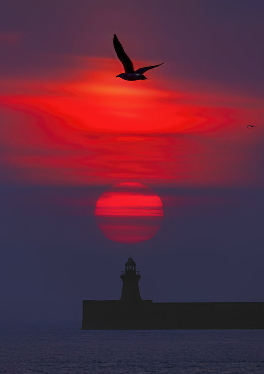Beautiful muted red sun over South Shields lighthouse.