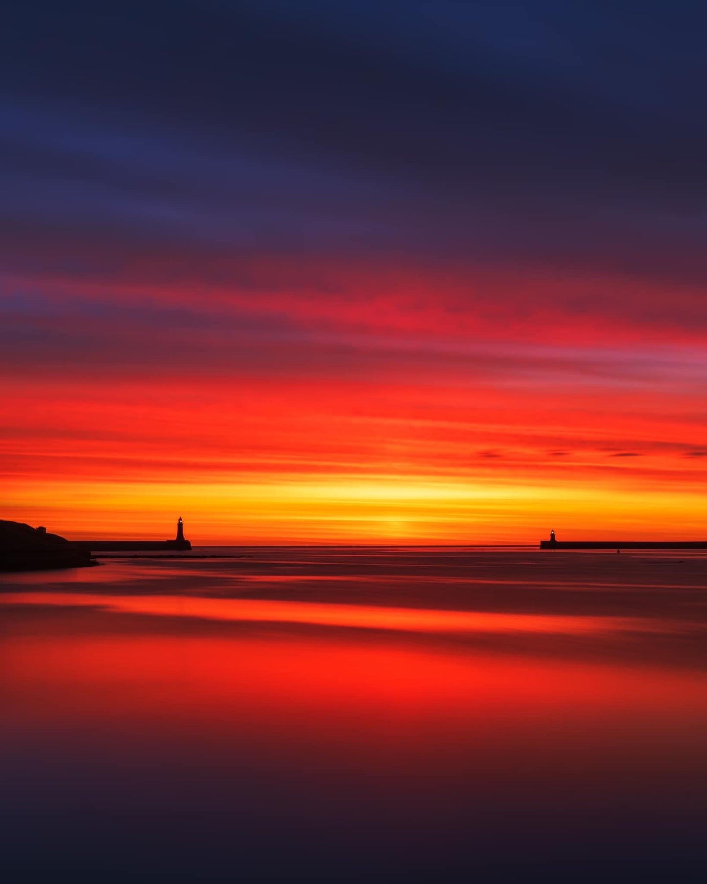 Fiery sunrise showing Tynemouth and South Shields lighthouses.