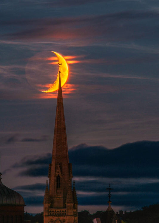 Crescent moon over a distant church.